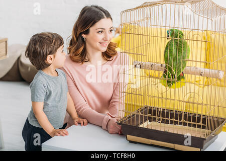 Jolie femme souriante avec son adorable perroquet vert dans la cage à oiseaux Banque D'Images