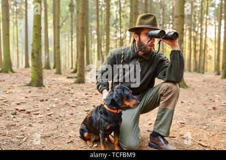 Chasseur ou le garde forestier de district avec hound comme un chien de chasse et de jumelles en attente dans l'Ansitz Banque D'Images