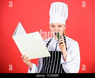 Faim. menu du restaurant. Suivre un régime culinaire. Femme au foyer avec. Livre de cuisine chef professionnel dans la cuisine manger du concombre. Cuisine. Femme au chapeau et un tablier cook. happy woman la cuisson des aliments sains par recette. Banque D'Images