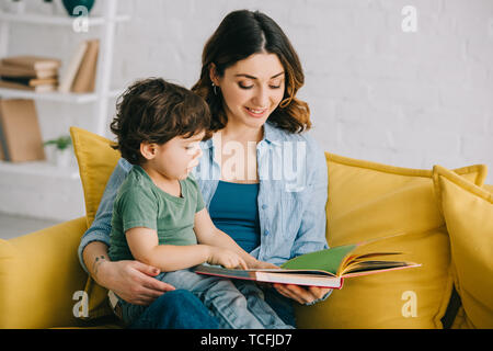 Maman et son fils assis sur le canapé jaune et reading book Banque D'Images