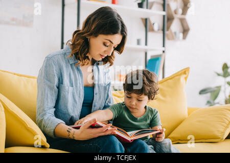 Maman et son fils assis sur le canapé jaune et reading book Banque D'Images
