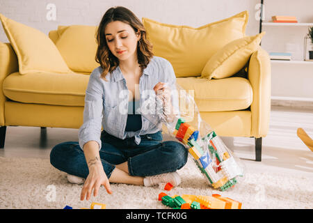 Tired woman en jeans assis sur un tapis avec des blocs de jouets Banque D'Images