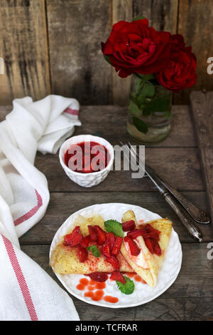 Crêpes minces avec la crème et sauce aux fraises sur une table en bois. De style rustique, selective focus. Banque D'Images