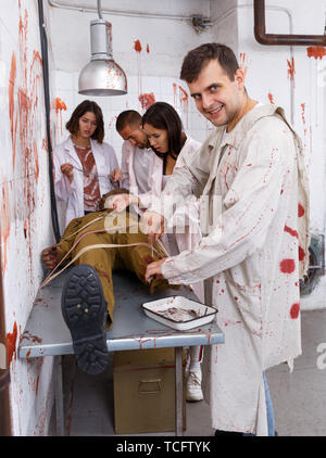 Guy avec folie zombie debout sur mannequin avec les amis en quête de style salle de chirurgie comme abandonné avec des traces de sang Banque D'Images