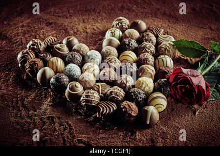 Coeur en chocolat Pralines de luxe l'arrangement pour la Saint-Valentin avec une rose rouge pour l'amour sur un fond de poudre de cacao avec Banque D'Images