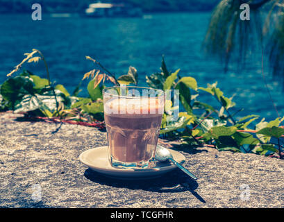 Image de verre de cafe latte sur un mur de pierre avec de l'eau dans l'arrière-plan Banque D'Images