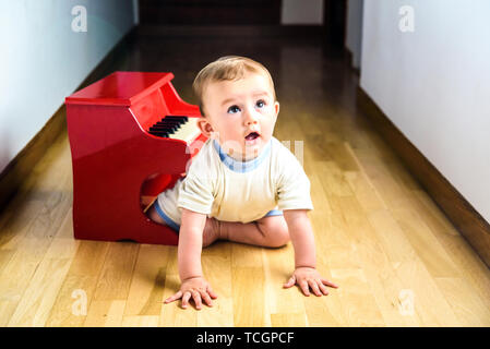 Bébé d'apprendre à jouer du piano avec un instrument, un jouet en bois tendre et drôle de scène de la petite enfance. Banque D'Images