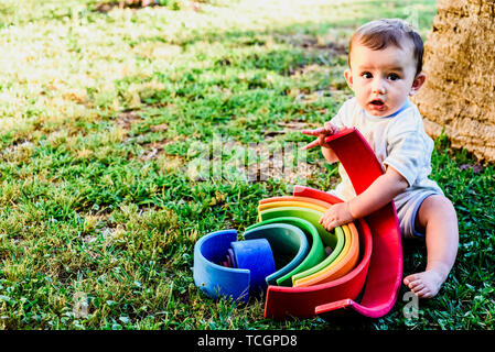 Bébé jouant avec un arc-en-ciel en bois coloré sur l'herbe, des droits de propriété intellectuelle et le développement mental. Banque D'Images