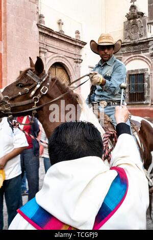 Un prêtre catholique bénit un cowboy sur son cheval au cours de la bénédiction annuelle des animaux pendant la fête de San Antonio Abad à l'Oratorio de San Felipe Neri Eglise dans le centre historique de San Miguel de Allende, Guanajuato, Mexique. Banque D'Images