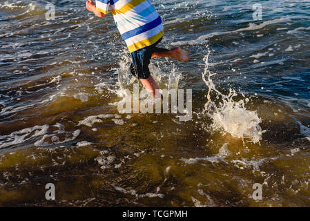 Enfant d'exécution sur le sable de la plage avec des vagues éclaboussant en été.