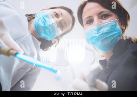 Vue de dessous de deux femmes dentistes dans le masque chirurgical et outils de maintien à l'appareil photo à. Point de vue du patient au dentiste. Banque D'Images