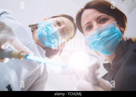 Vue de dessous de deux femmes dentistes dans le masque chirurgical et outils de maintien à l'appareil photo à. Point de vue du patient au dentiste. Banque D'Images