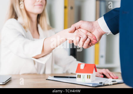 Vue partielle de smiling woman shaking hands with realtor près de house model on table Banque D'Images