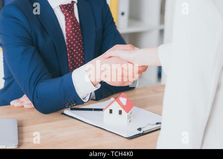 Vue partielle de client shaking hands with realtor près de house model Banque D'Images