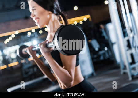 Selective focus of young woman working out avec haltères lourds in gym Banque D'Images