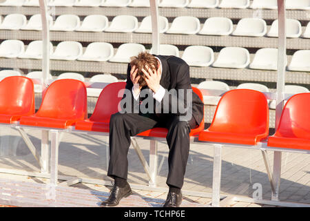 Entraîneur frustré assis sur chaise rouge ligne couvrant sa tête avec ses mains Banque D'Images