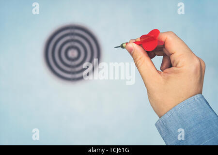 Dart rouge dans l'homme de main de point cible sur le mur bleu, selective focus on cible dart, concept de gagner. une main d'homme lance une fléchette sur la cible. Banque D'Images