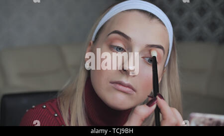 Une fille blonde s'applique le maquillage pour ses paupières. Banque D'Images