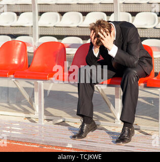 Entraîneur frustré assis sur chaise rouge couvrant sa tête avec ses mains Banque D'Images