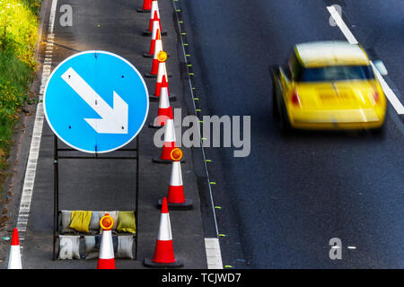 UK Route Services Travaux des cônes et des panneaux sur l'autoroute avec une voiture passe jaune. Banque D'Images