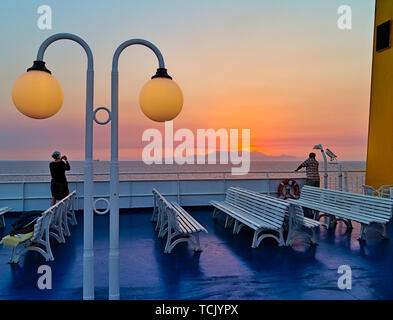 Jeune femme sur le navire taking photograph le coucher de soleil derrière l'île lointaine, montagnes, Mer Égée, Grèce. Banque D'Images