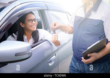 Asian Woman sitting in the broken voiture les clés donnant au mécanicien de voiture ou d'avion pour l'entretien dans le garage. Banque D'Images