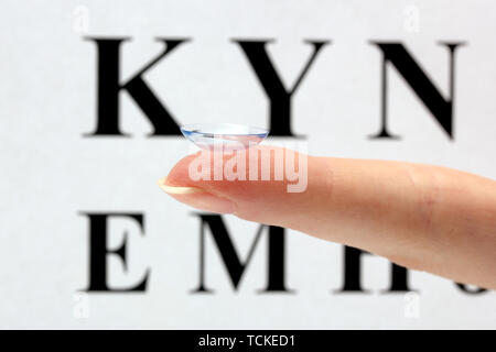 Sur le doigt de lentilles de contact, sur l'échelle Snellen eye fond du graphique Banque D'Images