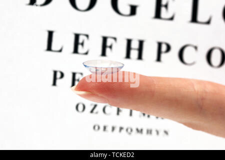 Sur le doigt de lentilles de contact, sur l'échelle Snellen eye fond du graphique Banque D'Images