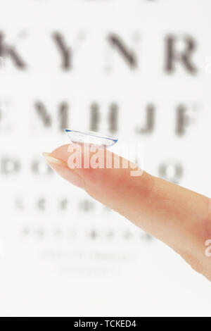 Sur le doigt de lentilles de contact, sur l'échelle Snellen eye fond du graphique Banque D'Images