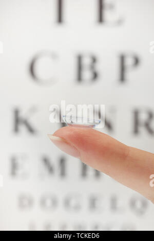 Sur le doigt de lentilles de contact, sur l'échelle Snellen eye fond du graphique Banque D'Images