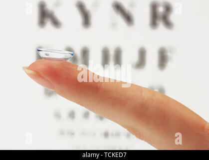 Sur le doigt de lentilles de contact, sur l'échelle Snellen eye fond du graphique Banque D'Images