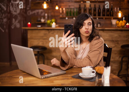 Cheerful young woman winking un l'appareil photo dans un café. Funny Girl à l'appareil photo du téléphone. Yung girl une journée décontractée dans un café. Banque D'Images