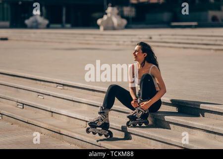 Vue de profil d'une femme assise sur le trottoir et la plaçant sur patins Banque D'Images