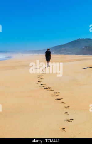 Lone man walking along beach laissant une traînée d'empreintes de pas dans le sable Banque D'Images