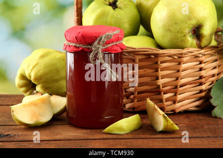 Pot de confiture et coings avec des feuilles dans le panier, sur fond vert Banque D'Images