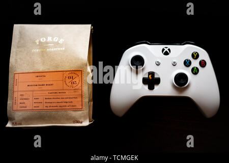 Un contrôleur de jeux Xbox s'assit à côté d'un sac de café contre un fond noir foncé Banque D'Images