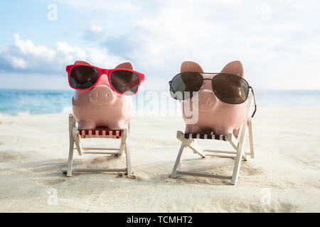 Lunettes de soleil rose sur la Piggybanks deux chaises miniatures sur la plage de sable Banque D'Images