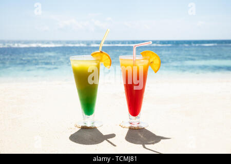 Deux verres de cocktails colorés sur la plage de sable contre le ciel bleu Banque D'Images