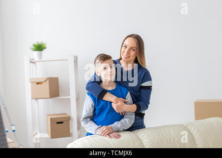 Smiling mother positive et charmant fils posent debout dans un nouvel appartement confortable lumineux. Le concept de déménagement et d'hypothèques pour les nouveaux Banque D'Images