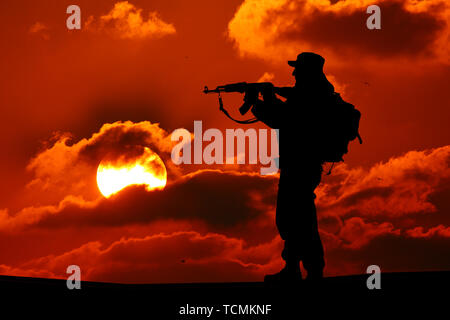 Silhouette de soldat ou l'officier militaire avec des armes au coucher du soleil. shot, holding gun, coloré ciel, la montagne, l'arrière-plan Banque D'Images