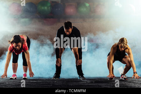 Groupe d'amis adolescents ou les sportifs de l'exercice et faisant s'accroupit au centre crossfit Banque D'Images