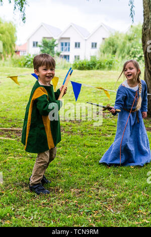 Le week-end médiéval. Portrait de deux jeunes enfants, garçon, 4-5 ans, et une fille, 5-6 ans, vêtu de vêtements médiévaux et des combats à l'épée et espièglerie ax dans l'herbe avec saule derrière. Banque D'Images