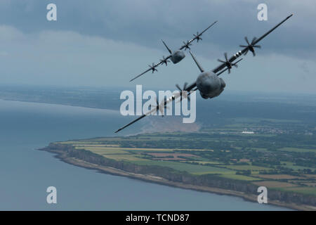 Deux C-130J Super Hercules, appartenant au 37e Escadron de transport aérien sur la base aérienne de Ramstein, voler plus de Pointe-du-Hoc dans le cadre d'une formation à quatre appareils avec un C-17 Globemaster III de un mille derrière la formation en Normandie, France, le 5 juin 2019. Pointe-du-Hoc, les terres côtières dotée d''une falaise de 100 pieds donnant sur l'océan Atlantique, a fourni le plus haut poste d'observation entre les secteurs de débarquement américain à l'Utah et Omaha Beach le Jour J, le 6 juin 1944. L'armée allemande fortifiée Pointe-du-Hoc en conséquence. Malgré les défenses de l'axe, l'Armée américaine à l'échelle du Groupe d'Assaut Rangers le pied 100 cl Banque D'Images