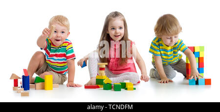 Adorables petits enfants jouant avec des jouets ou des blocs et de s'amuser tout en étant assis sur le plancher isolé sur fond blanc Banque D'Images