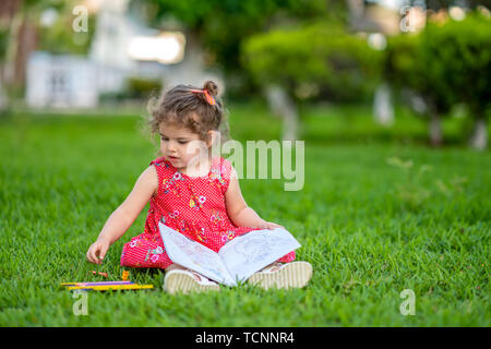 Petite fille d'apprentissage ou d'un dessin à colorier peindre sur l'herbe verte dans la nature au jardin. Banque D'Images