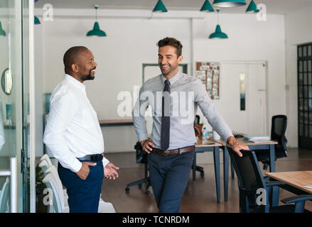 Close up image de deux hommes d'âge mûr parler et rire ensemble tout en se tenant dans un grand bureau moderne Banque D'Images