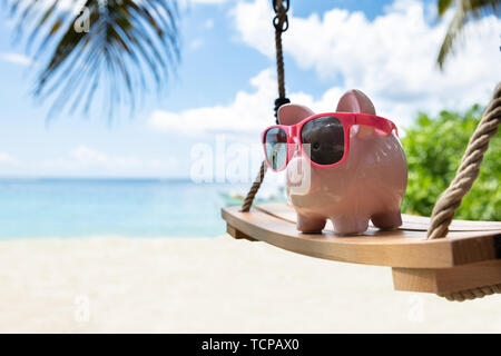 Close-up of Pink Piggybank With Sunglasses sur balançoire en bois At Beach Banque D'Images