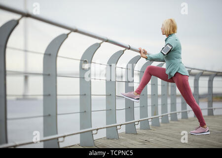 La sportive blonde, leggins en baskets et coupe-vent debout sur bridge par Riverside et de repos après l'entraînement en plein air Banque D'Images