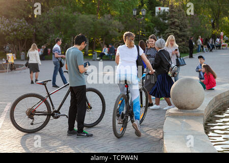 Un jeune couple d'hommes et de femmes de la bicyclette au cours d'une promenade dans le parc parmi un grand nombre de personnes sur un week-end sur une journée claire et chaude. Utile vacat Banque D'Images