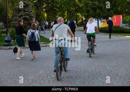 Couple de personnes âgées, hommes et femmes de la bicyclette au cours d'une promenade dans le parc parmi un grand nombre de personnes le week-end sur une chaude après-midi d'été. Utile Banque D'Images